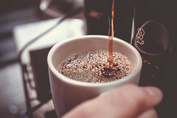 Hot coffee being dispensed into a white ceramic mug
