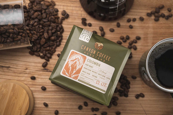 Flatlay image with spilled coffee beans, a mug of black coffee, and a bag of Canyon Coffee Roasters coffee