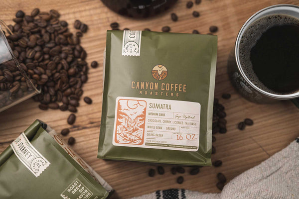 Flatlay image with spilled coffee beans, a full mug of coffee, and a bag of Canyon Coffee Roasters coffee