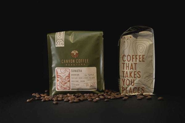 Two 16 ounce bags of Canyon Coffee Roasters coffee surrounded by roasted coffee beans